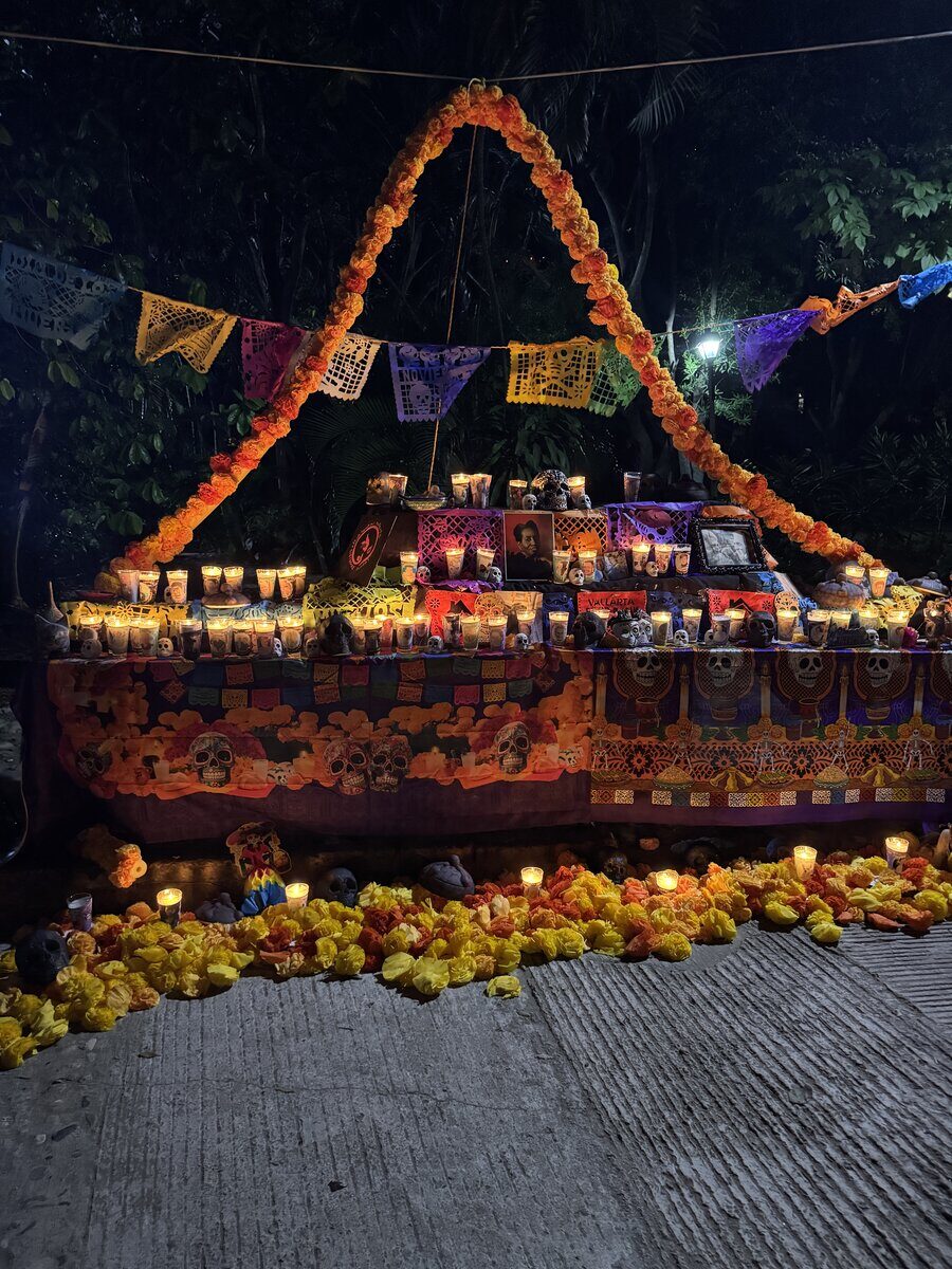 A public ofrenda at night under an arch of marigolds, with papel picado and candles