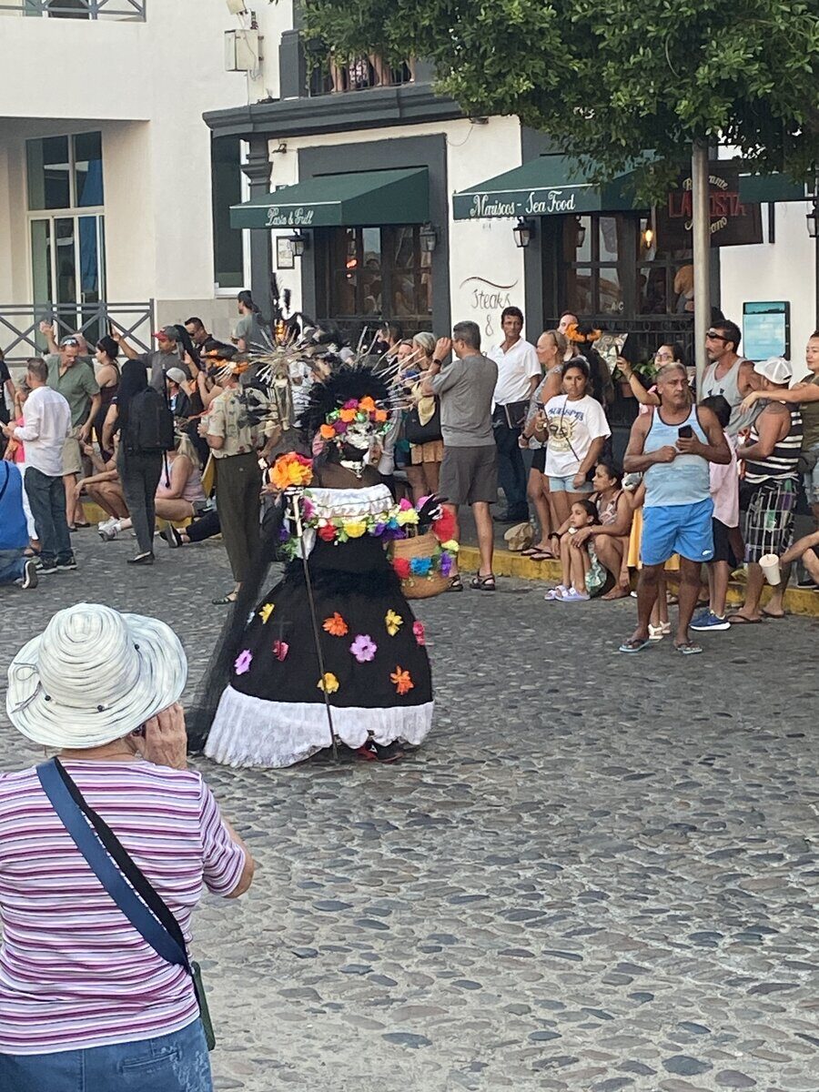 A Catrina performer walking through a crowded cobblestone street during a Día de los Muertos parade in Centro