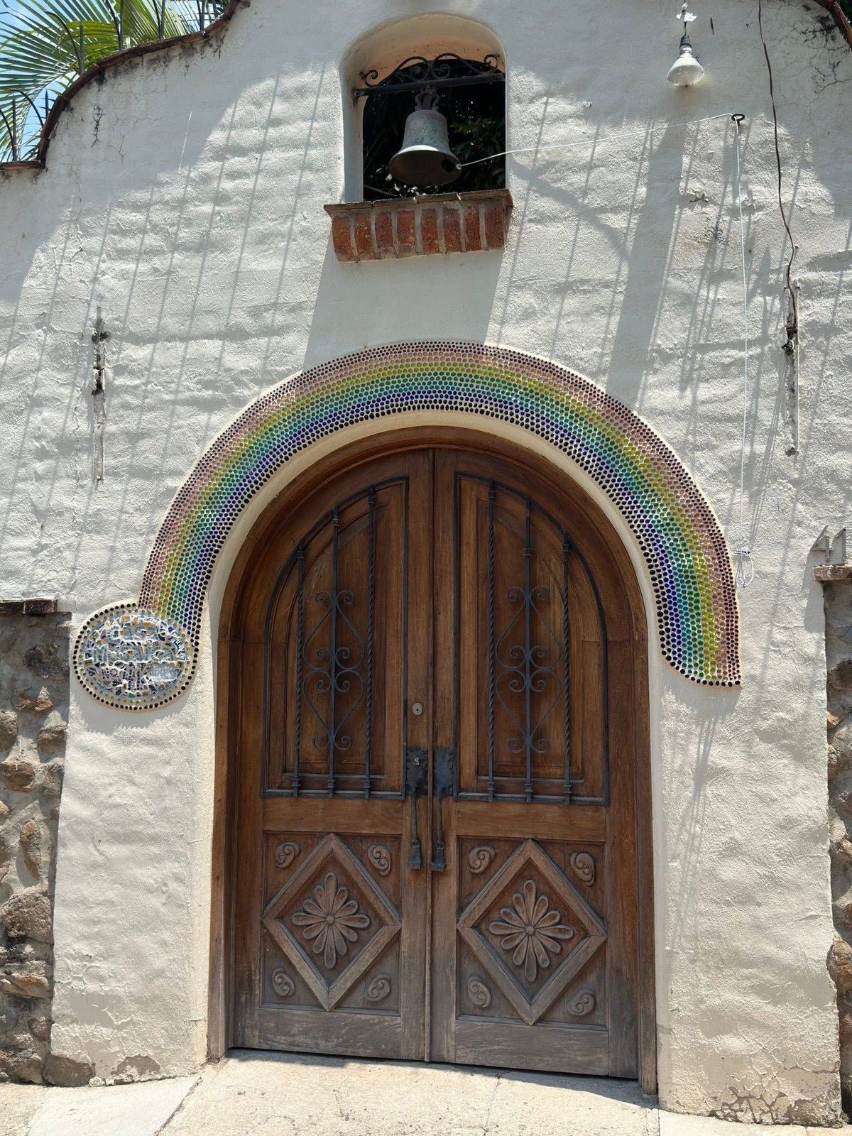 Arched wooden front door with a rainbow tile arch and a small bell in Puerto Vallarta