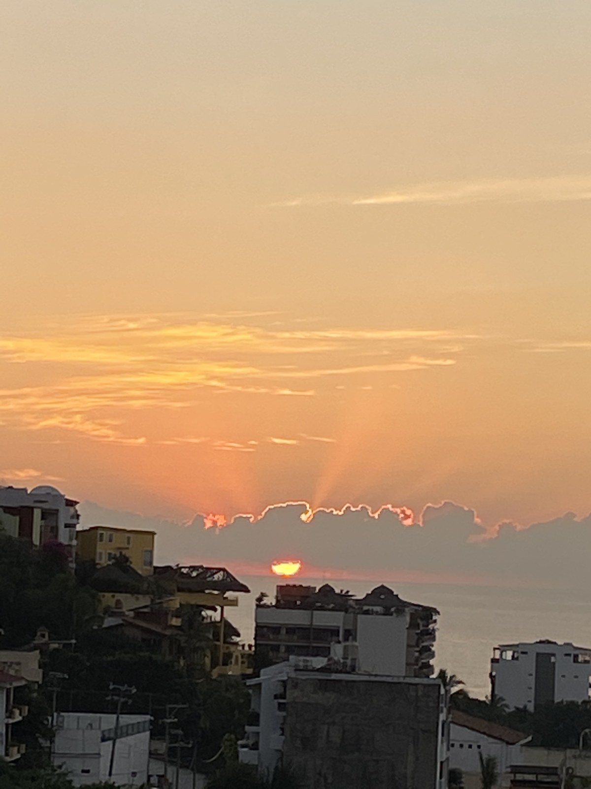 Sun rays breaking through clouds at sunset over the rooftops and sea in Puerto Vallarta