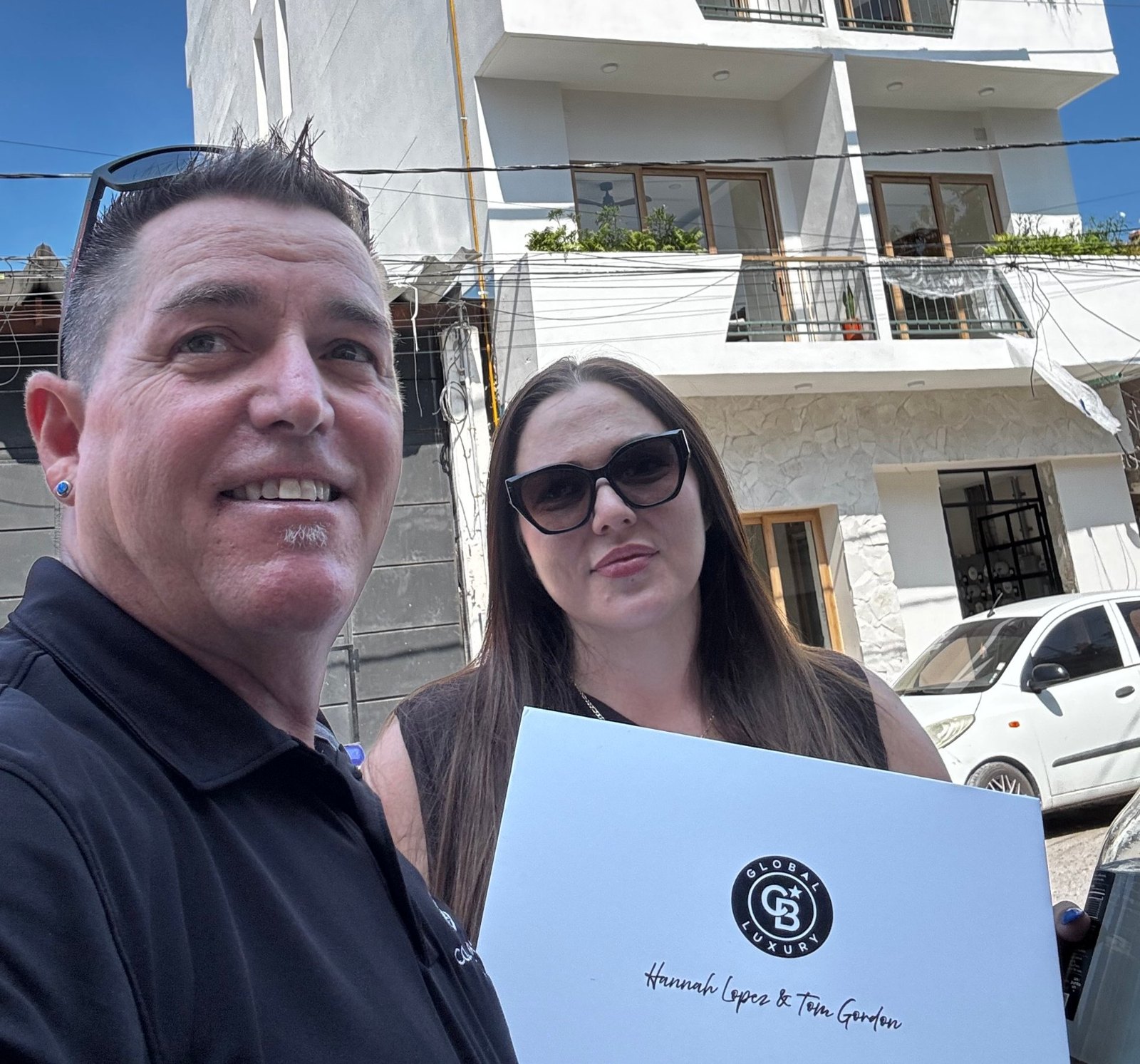 Hannah López and Tom Gordon holding a Coldwell Banker Global Luxury gift box in front of Trópico in Puerto Vallarta