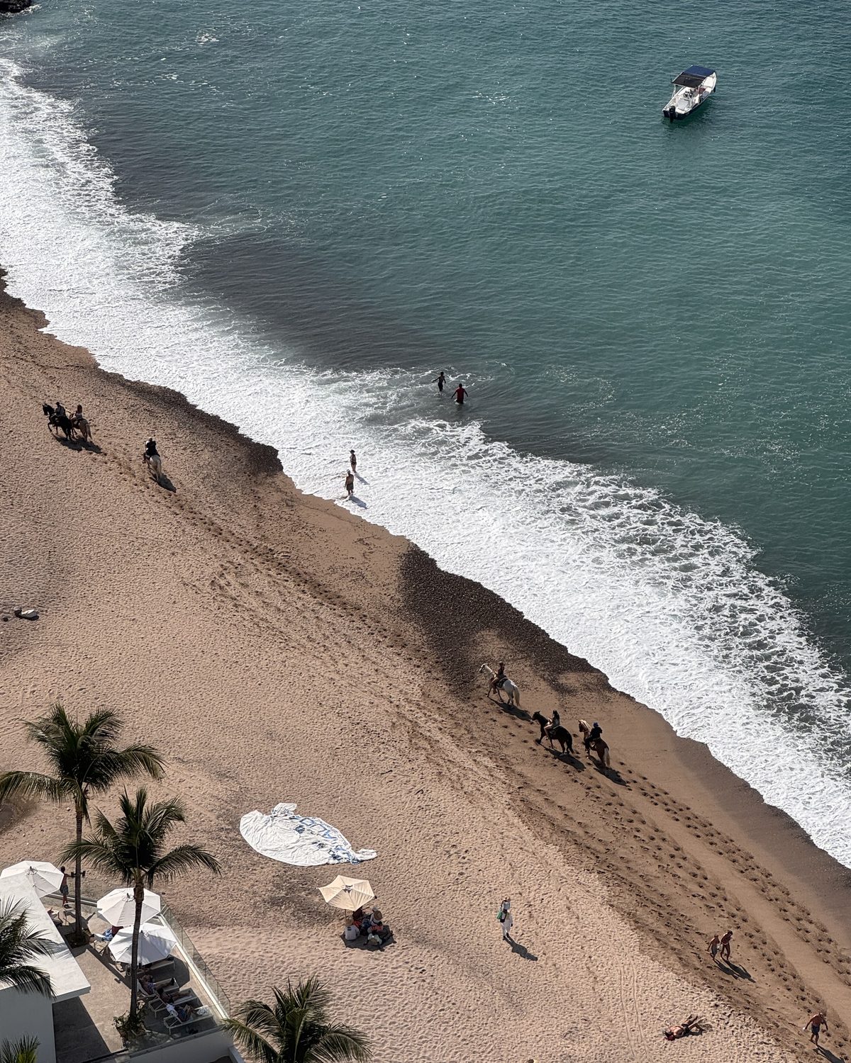 Looking straight down on the beach with horseback riders along the waterline