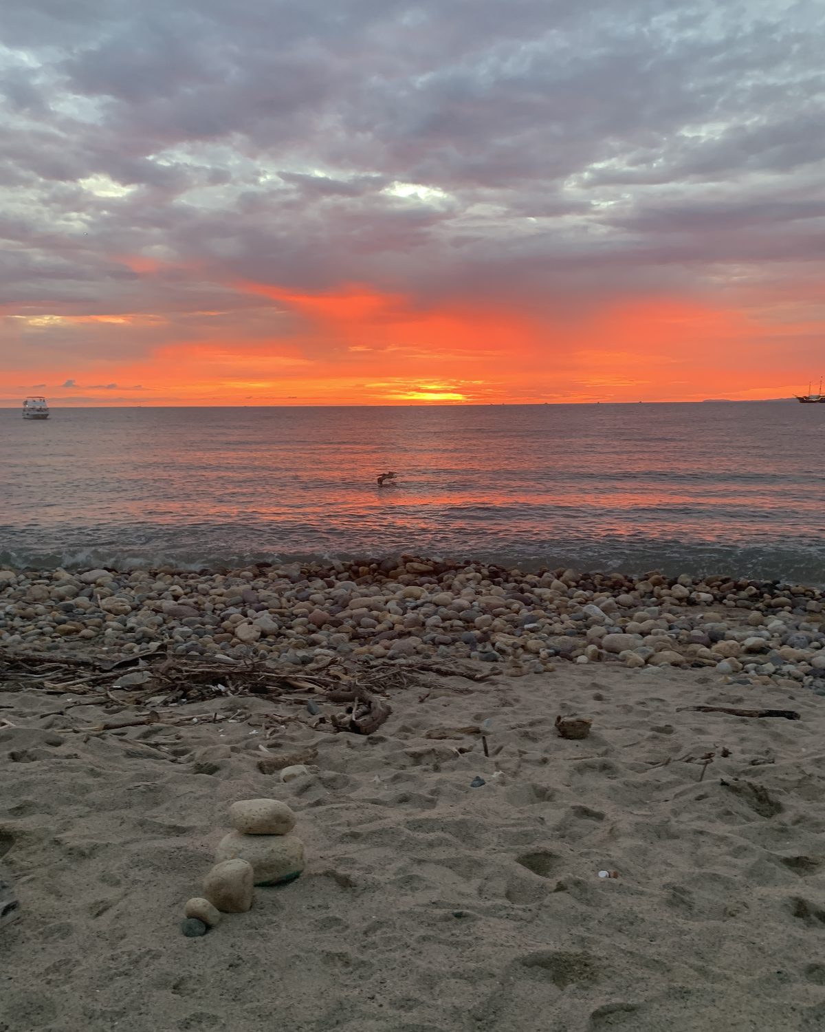 Sunset over the bay from a stretch of shore covered in stones