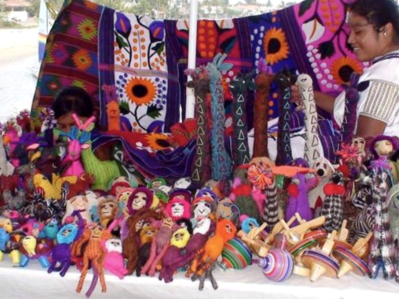 Handmade embroidered textiles and colorful dolls on an artisan's table at the La Cruz market