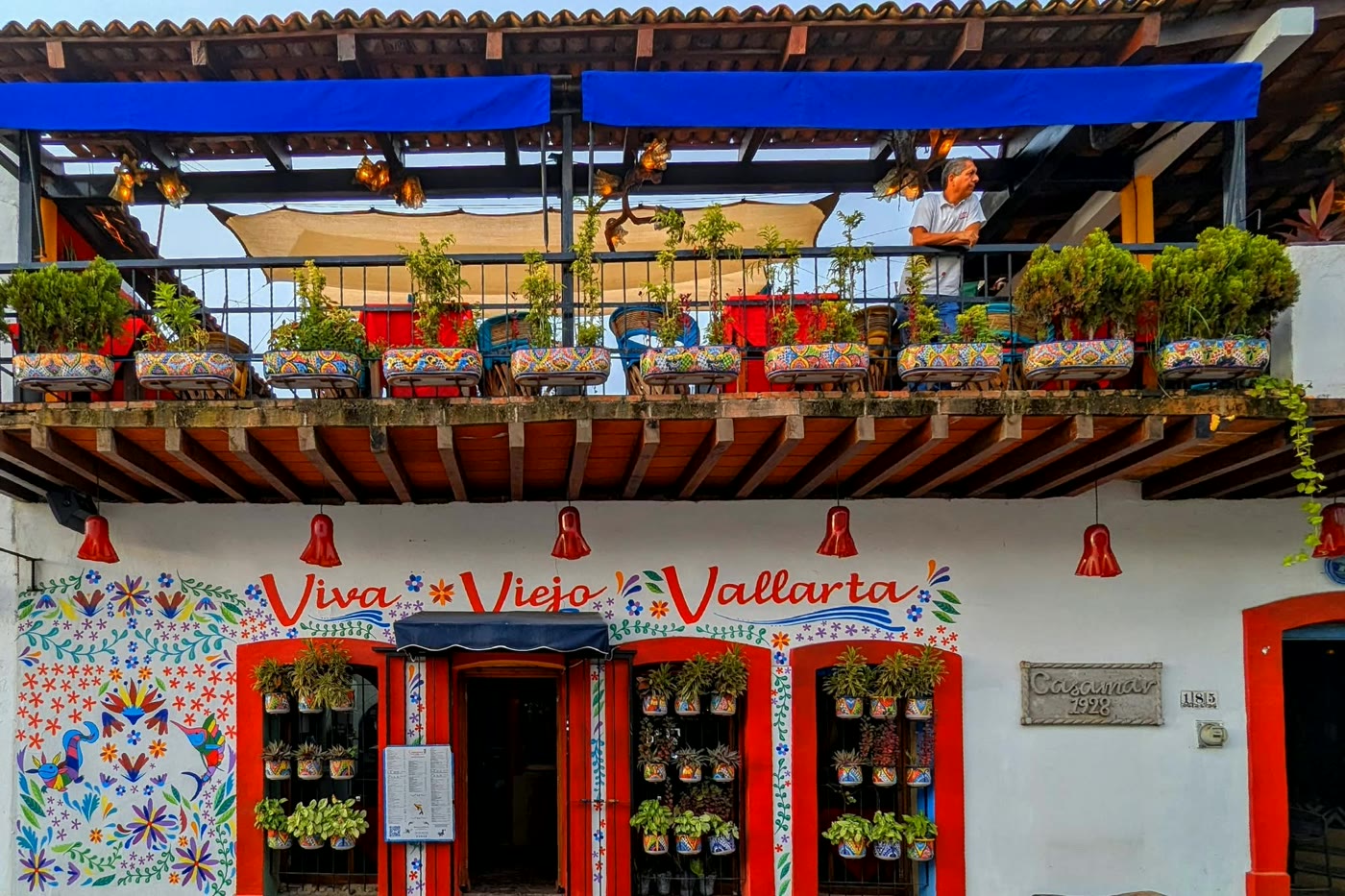 A hand-painted local restaurant front in Puerto Vallarta with folk-art flowers, planted balcony and a blue awning