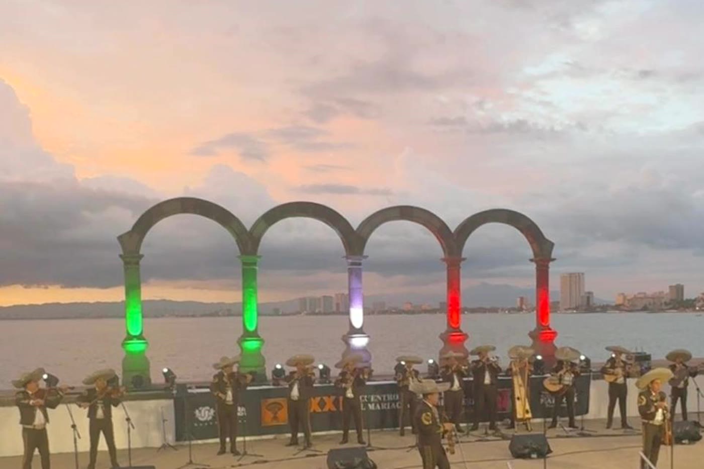 The Malec&oacute;n arches in Puerto Vallarta lit in green, white and red at dusk, with mariachis playing to a crowd