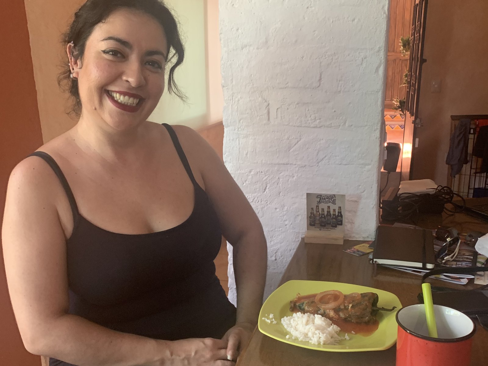 Karla smiling at a wooden table at Casa Tamarindo with a plate of chile relleno and rice in front of her