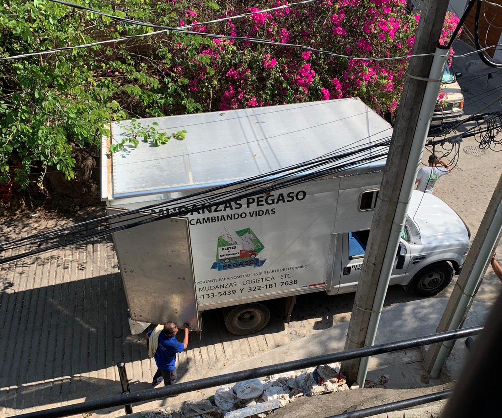 A Mudanzas Pegaso moving truck parked at the bottom of a stairway in Puerto Vallarta, bougainvillea above it, a mover opening the back doors