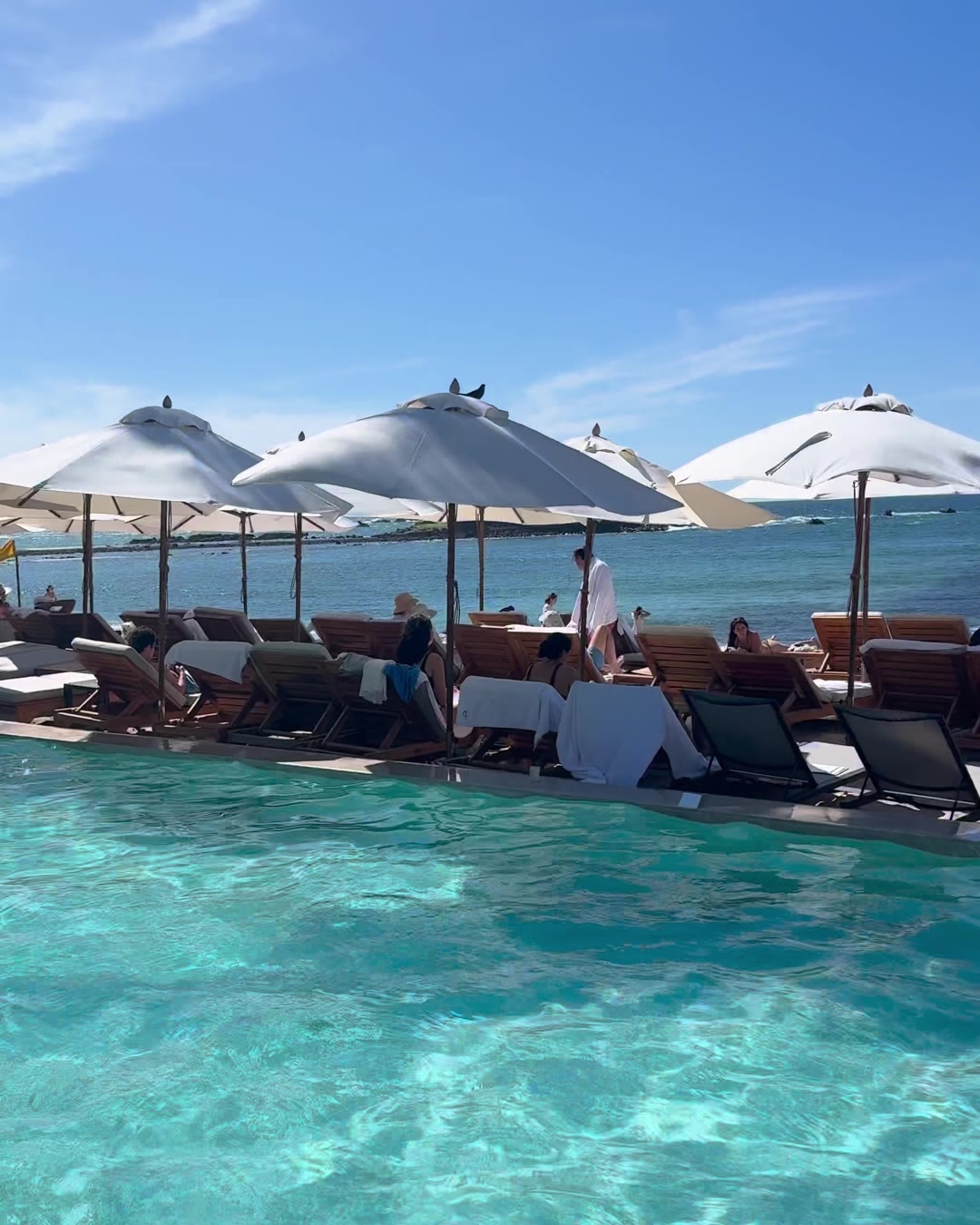 A beach club pool with white umbrellas and loungers facing the ocean in Punta Mita