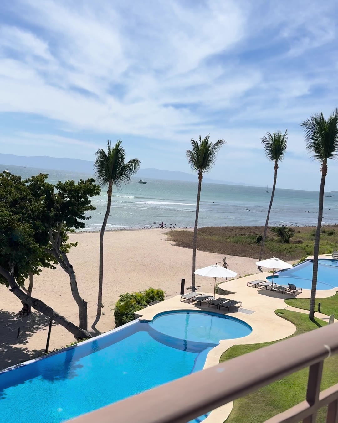Looking down from a balcony over palms, pools and a long sandy beach on the Punta Mita coast