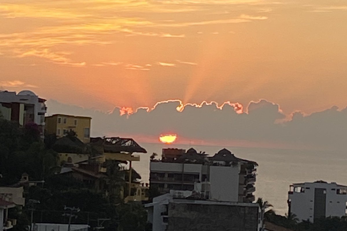 Sun rays breaking through clouds at sunset over the rooftops and sea in Puerto Vallarta