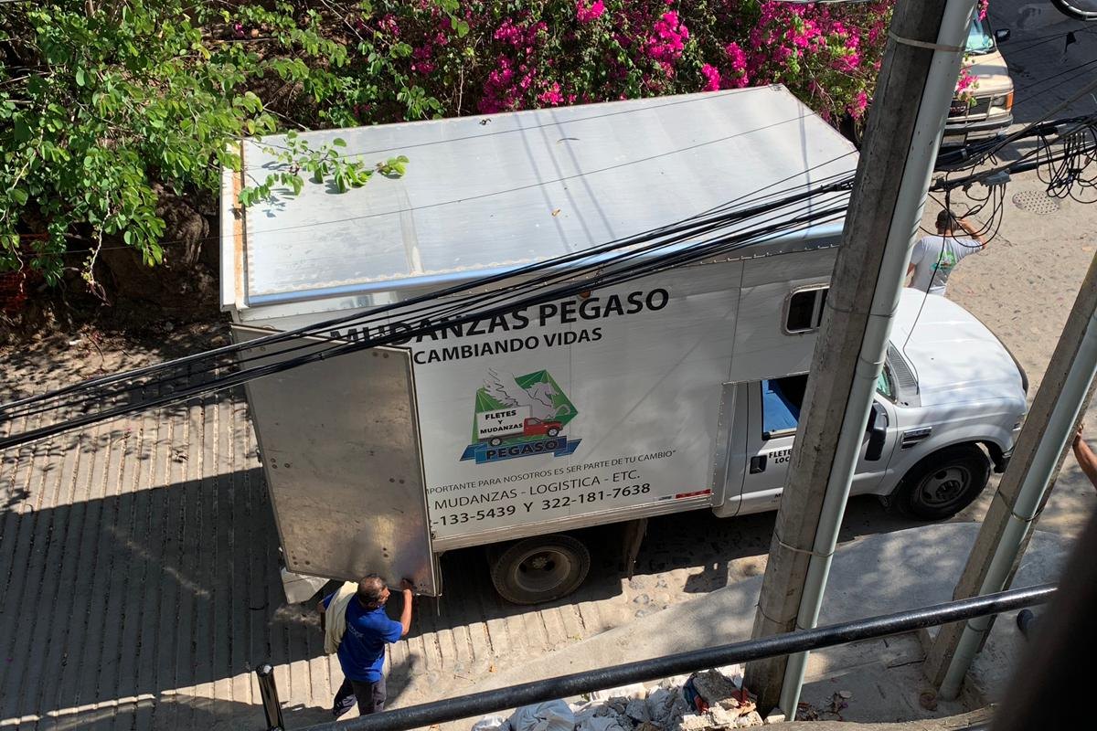 A moving truck parked at the bottom of a stairway in Puerto Vallarta under bougainvillea